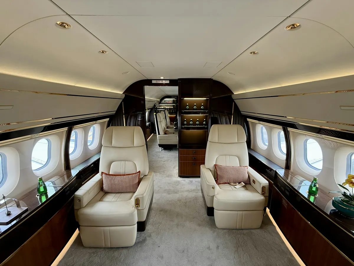Wide private jet cabin with two cream leather seats and a polished wood galley behind